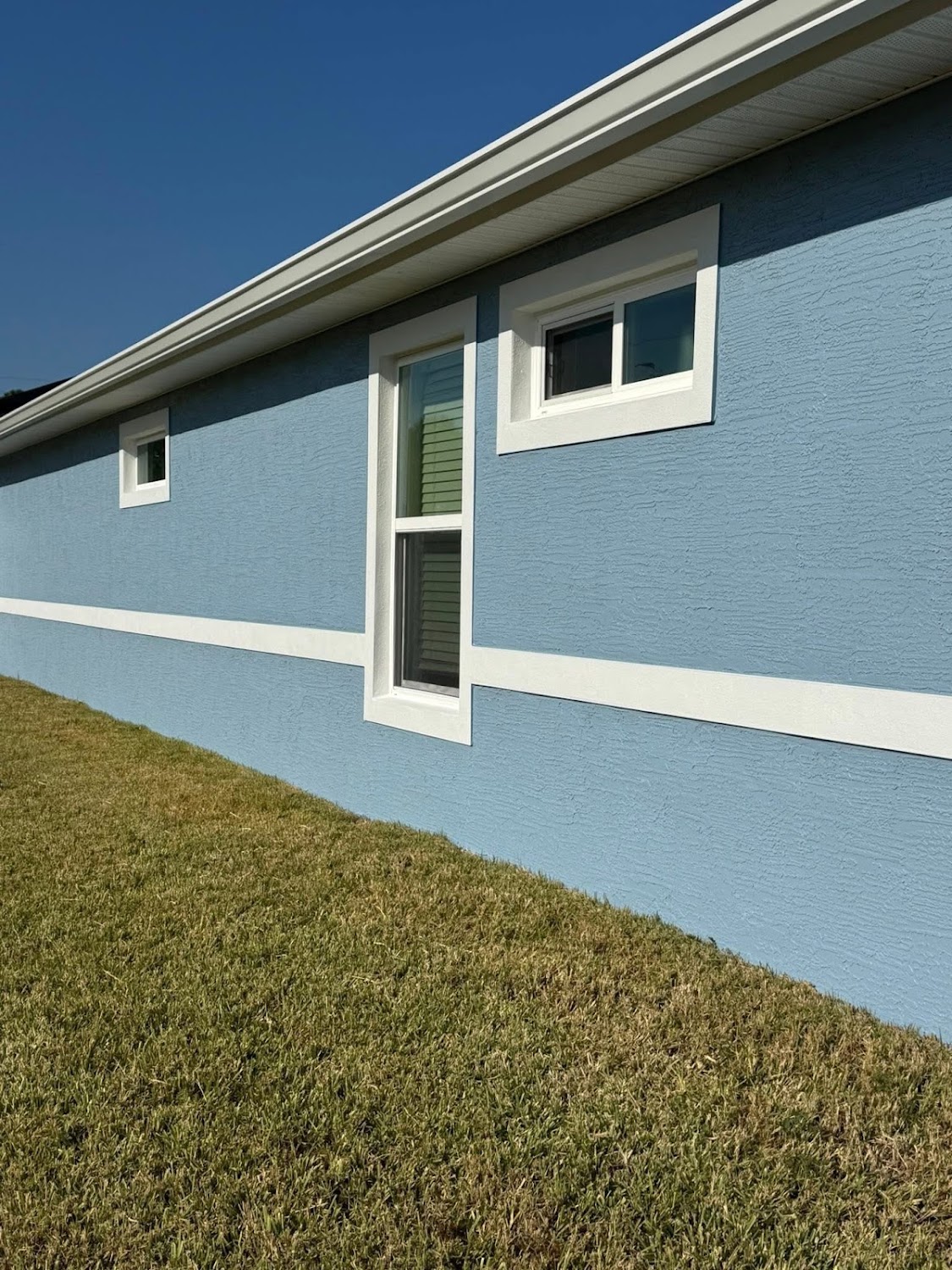 A home exterior painted powder blue with clean white trim and window frames on a bright day